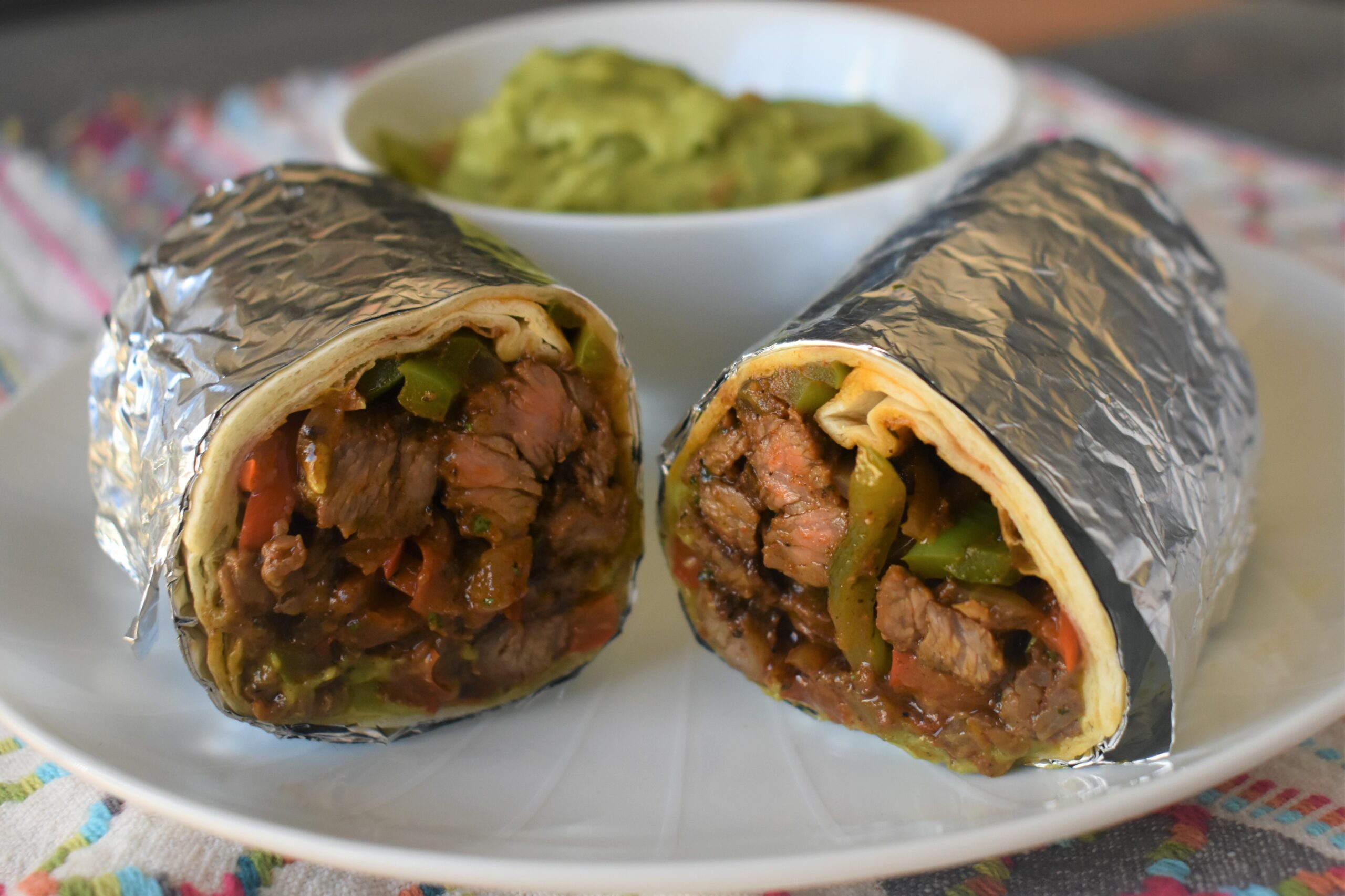 a plate with an albuquerquw burrito cut in half with a cup of guacamole