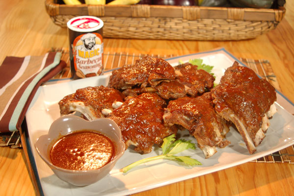 a plate of barbeque baby back ribs next to a container full of barbeque sauce for dipping