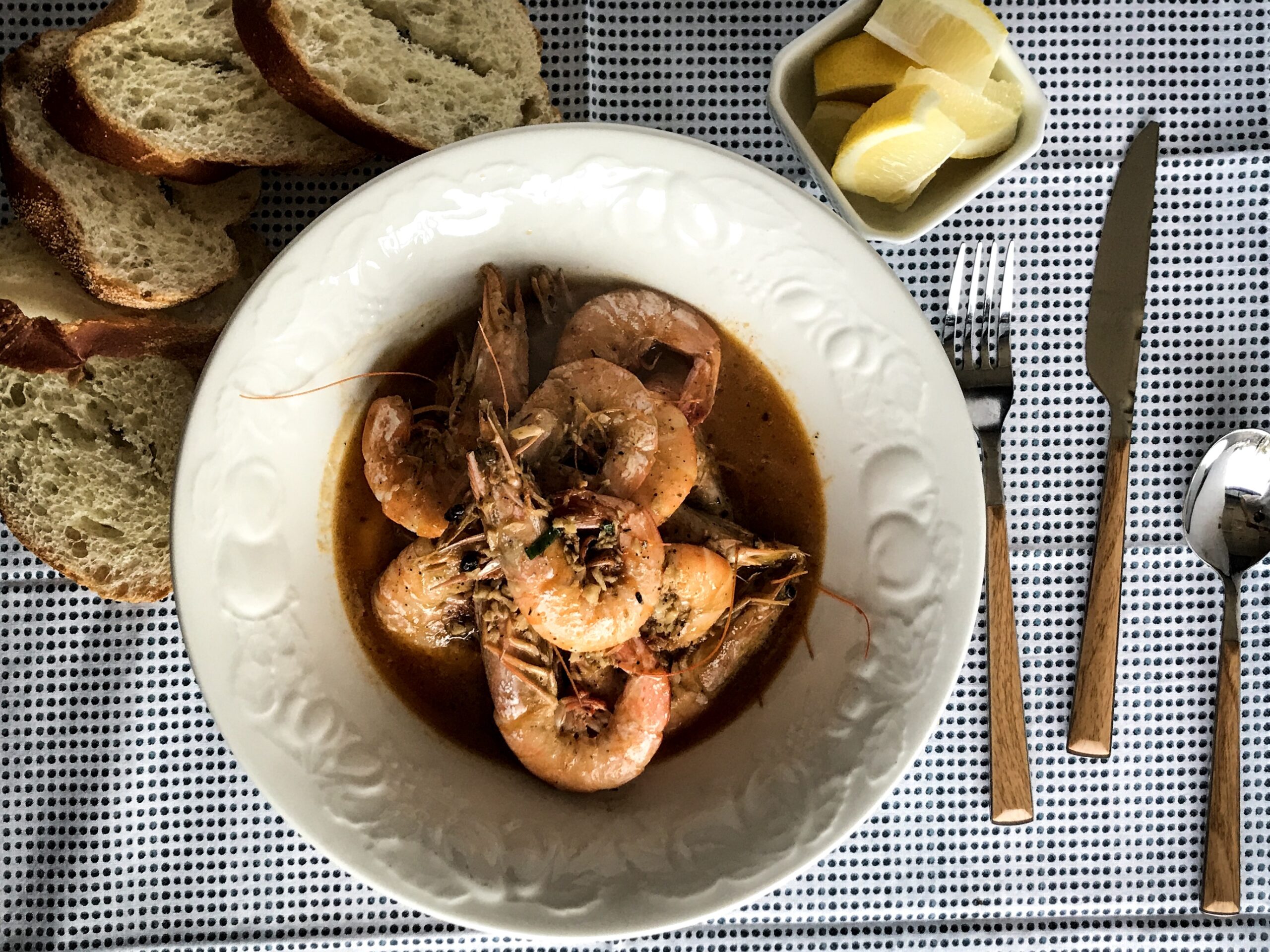 a plate with barbeque shrimp, some lemon slices and bread