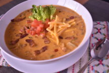 a close up of a blt soup topped with bacon, tomatoes, guacamole and shredded cheese
