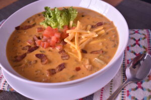 a close up of a blt soup topped with bacon, tomatoes, guacamole and shredded cheese