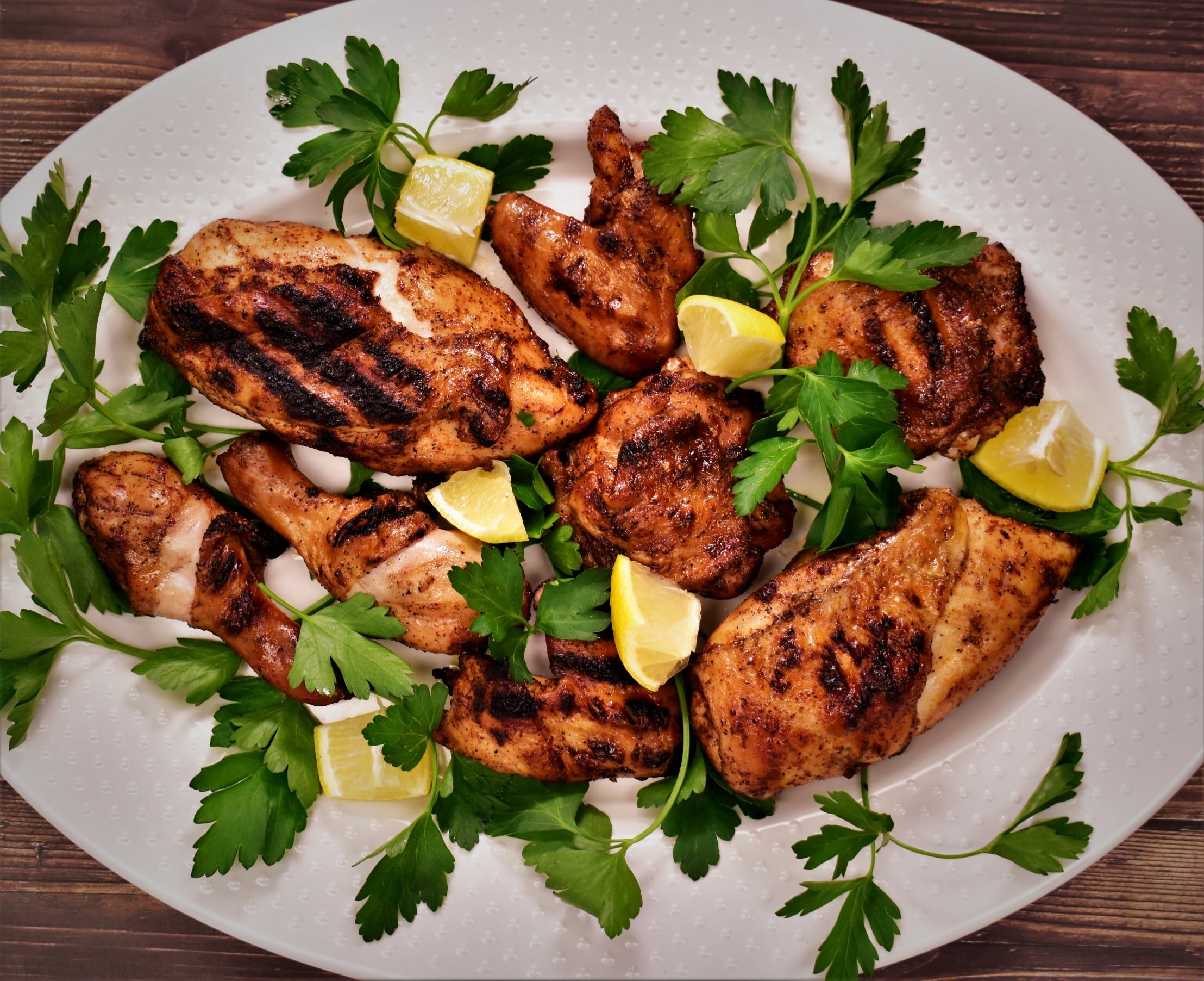a plate of barbecue magic rotated chicken with full basil leaves and lemon cubes for garnish
