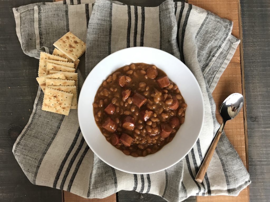 a bowl with barbeque beanie weenies with a handfull of crackers on the side