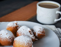 a plate with 5 Beignets next to a cup of coffee