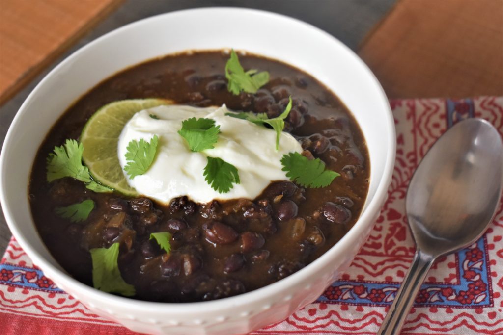 a bowl of black bean soup with a lime slice, a dollap of sour cream and basil on top