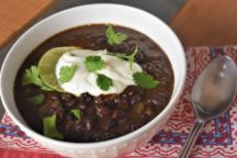 a bowl of black bean soup with a lime slice, a dollap of sour cream and basil on top