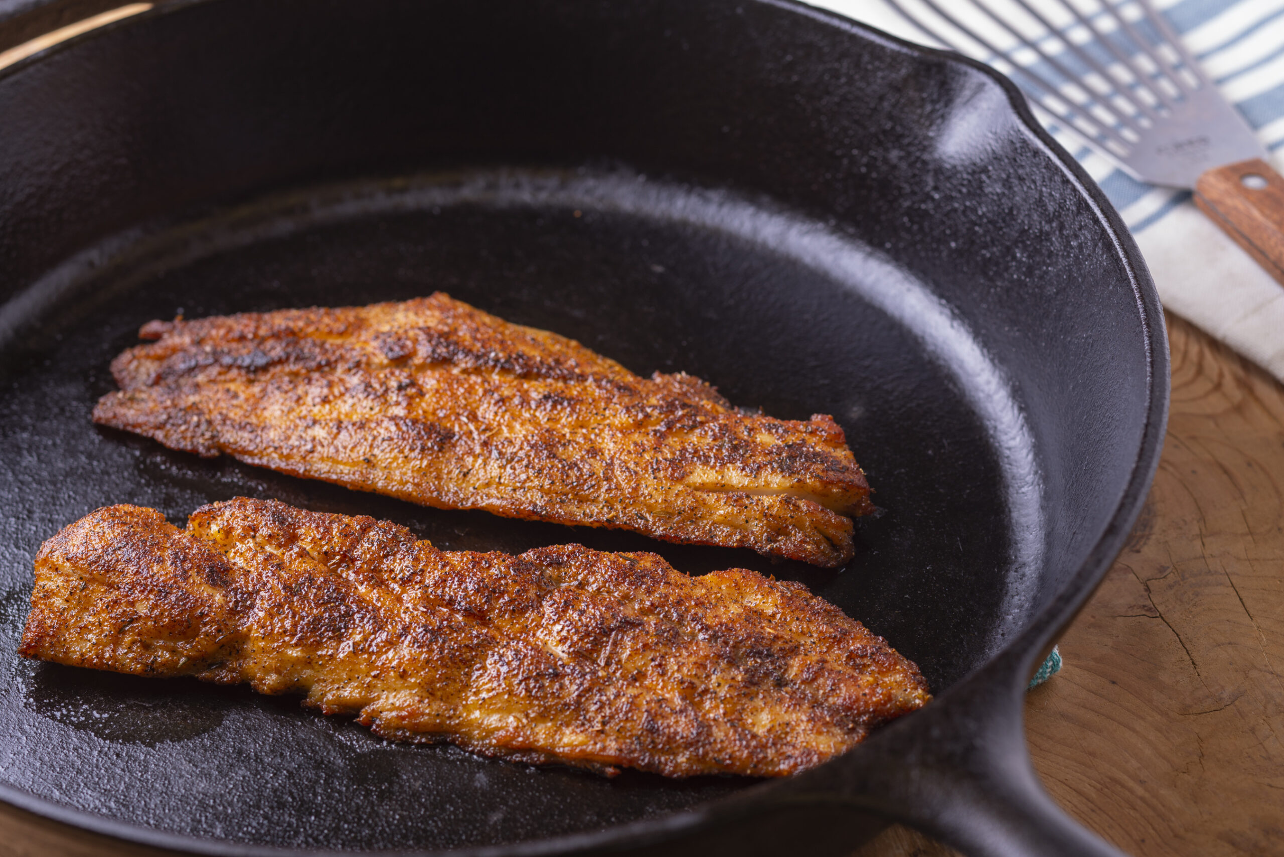 a cast iorn skillet with 2 pieces of blackend fish fillets cooking