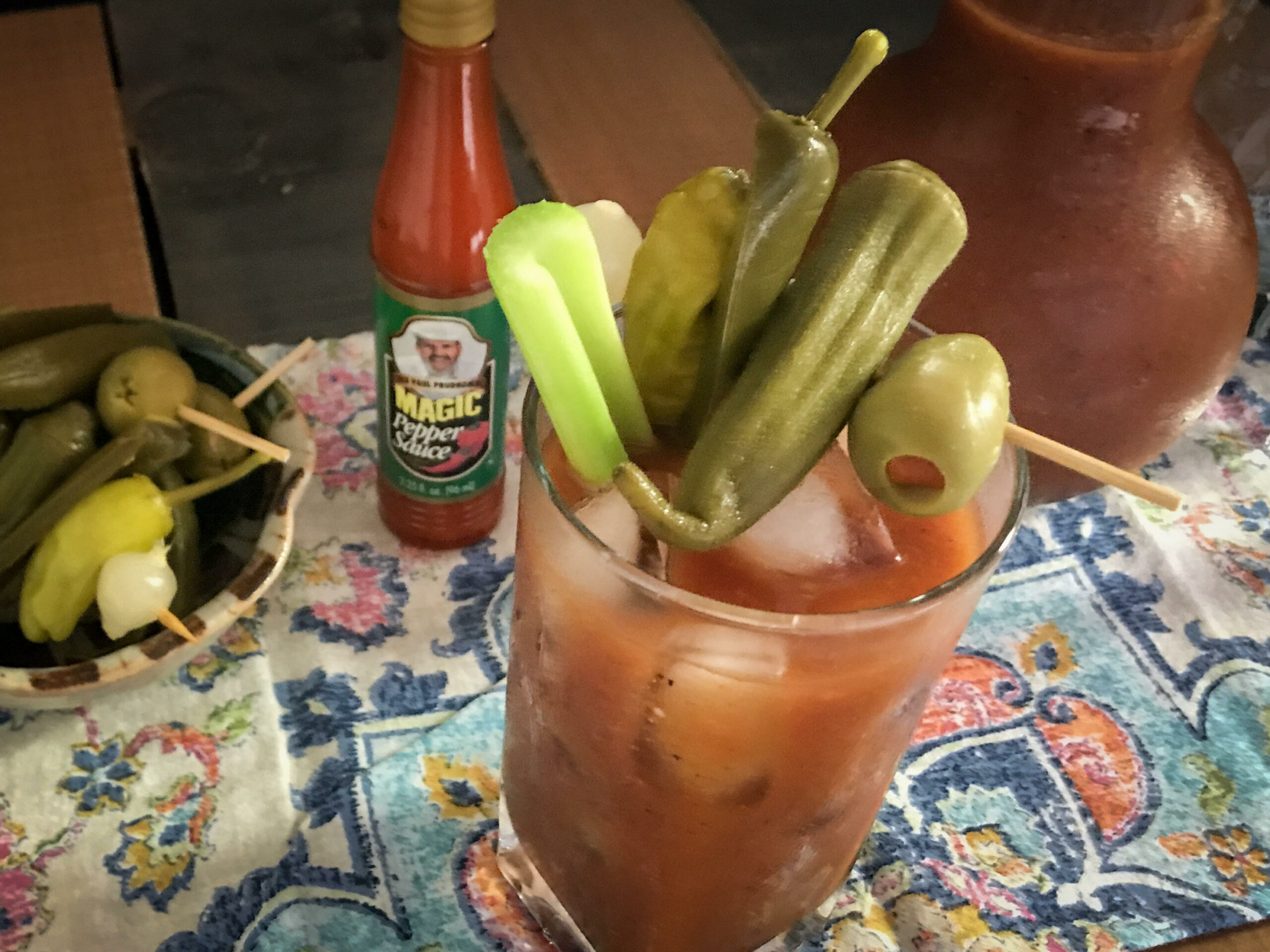 a drink glass full of bloody mary topped with 3 peppers, one olive and a celery stick
