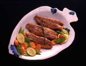 a fish shaped plate with 3 pieces of bronzed redfish and veggies