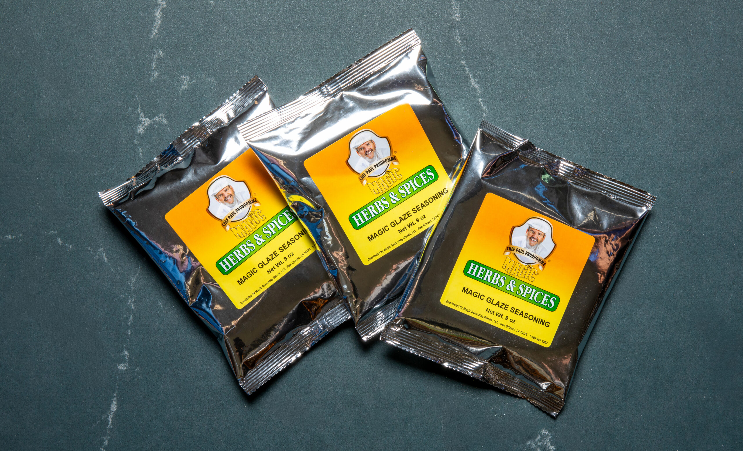 three silver pouches of chef paul prudhomme's magic glaze on a dark background