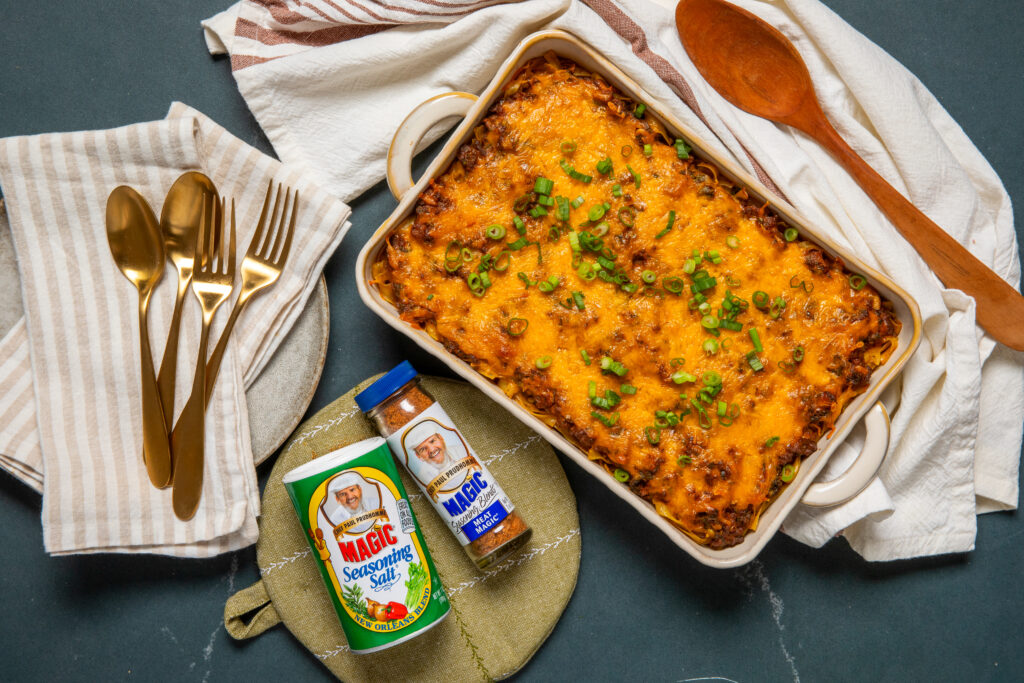 Beef Noodle Casserole in a white serving dish on a tea towel with seasoning next to it