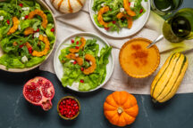 Salad on a plate next to a bigger plate of salad and pumpkins on a tea towel