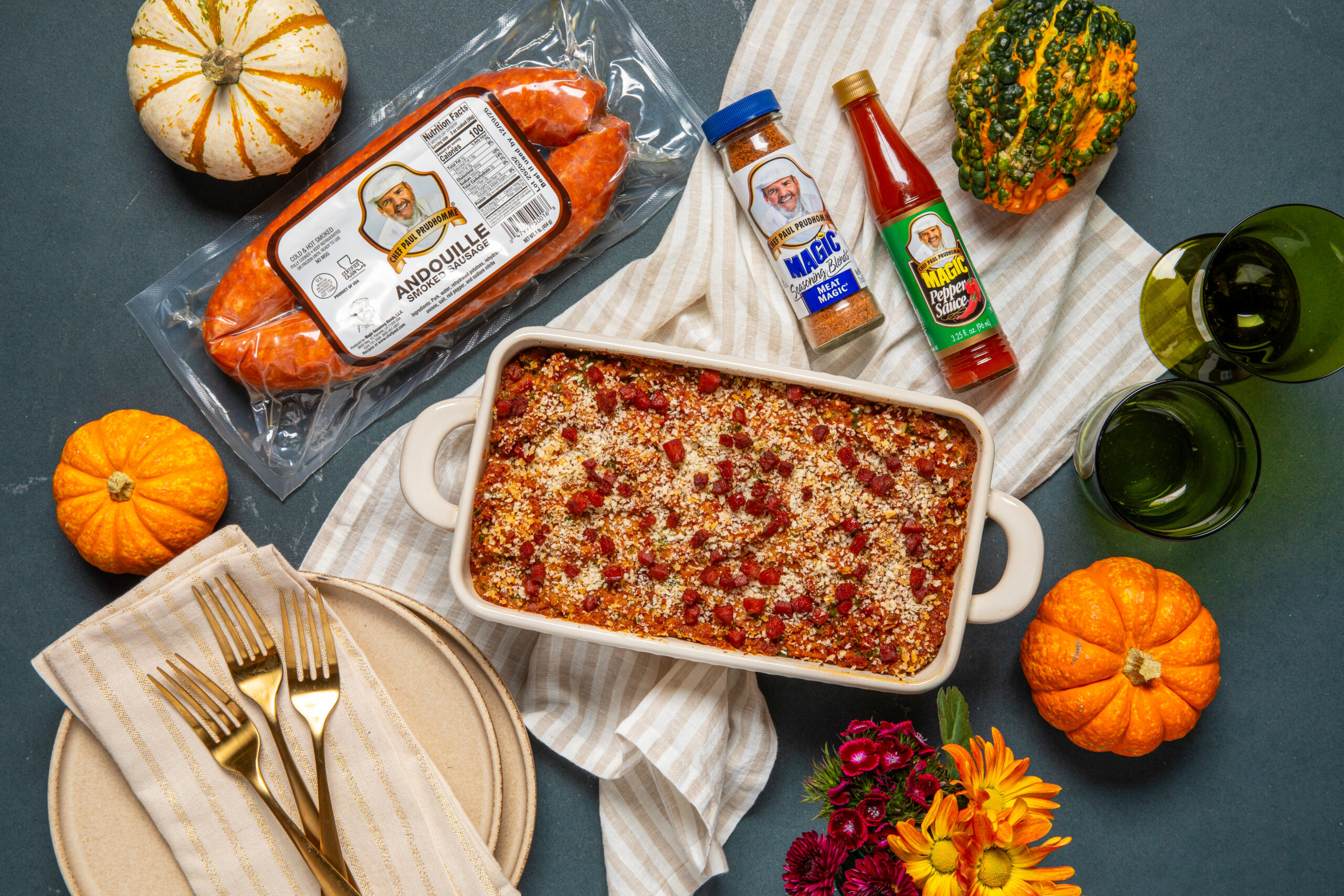 Andouille Sausage dressing in a serving dish with sausage, pepper sauce and seasoning next to it