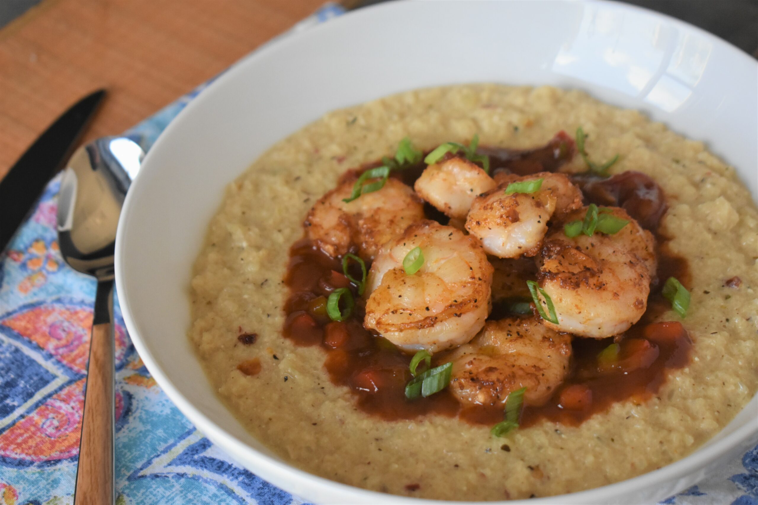 a bowl of creamy califlower cheese grits topped with shrimp and chopped green onions