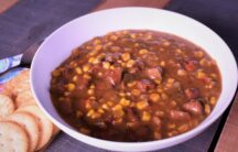 a bowl of corn and andouille soup next to some white crackers