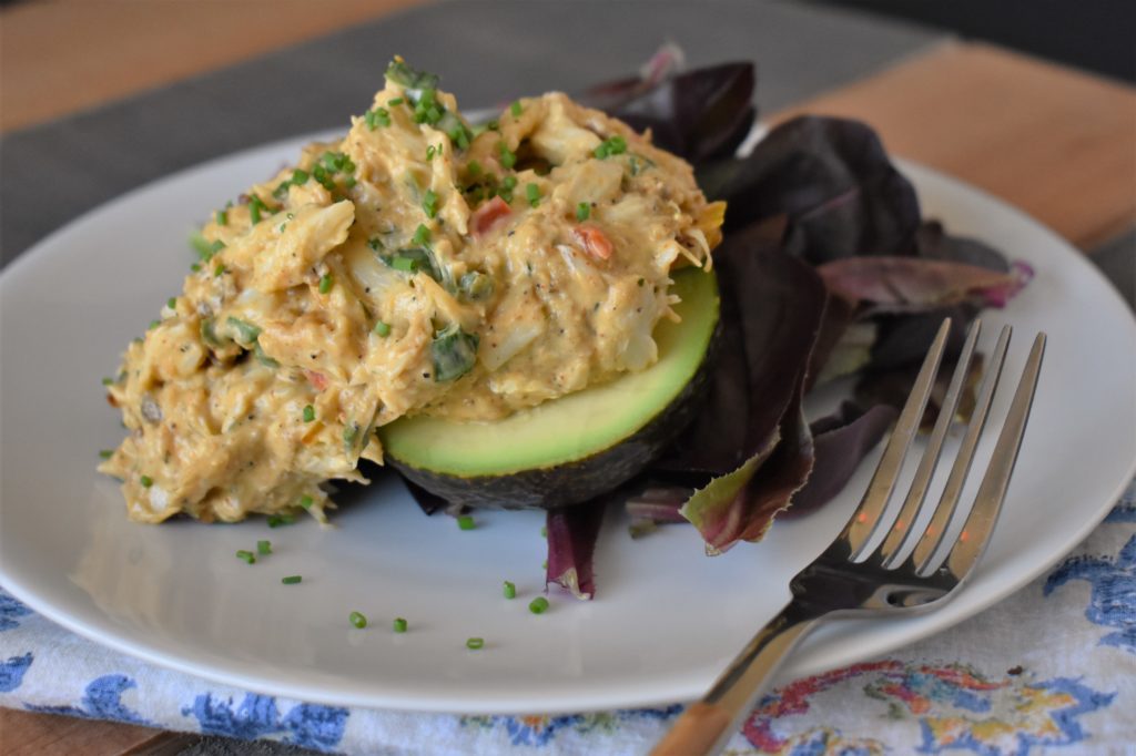 a plate with avovado stuffed with crabmeat salad with a side salad