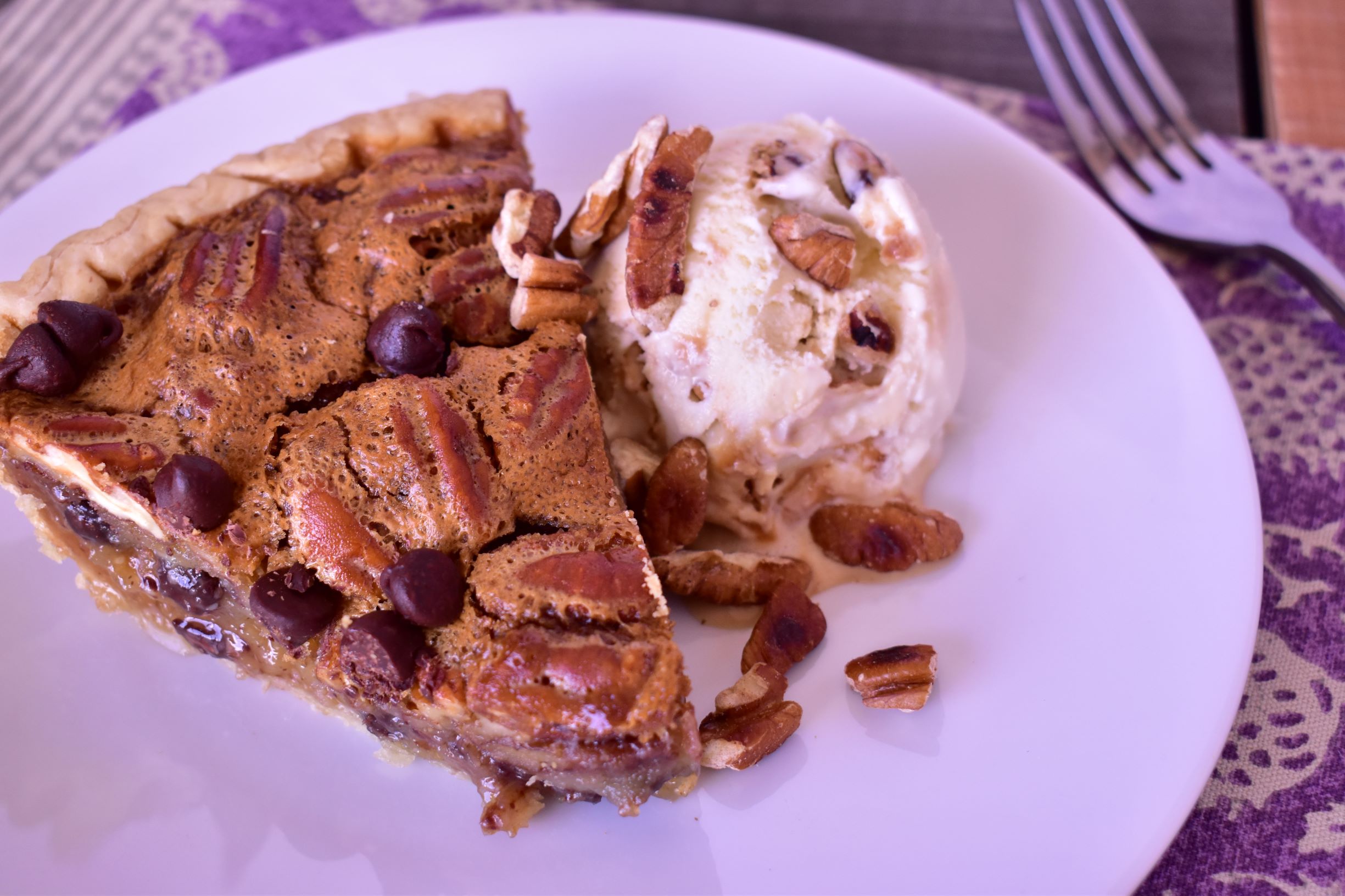 a plate with a piece of chocolate praline pie next to a scoop of buttered pecan ice cream