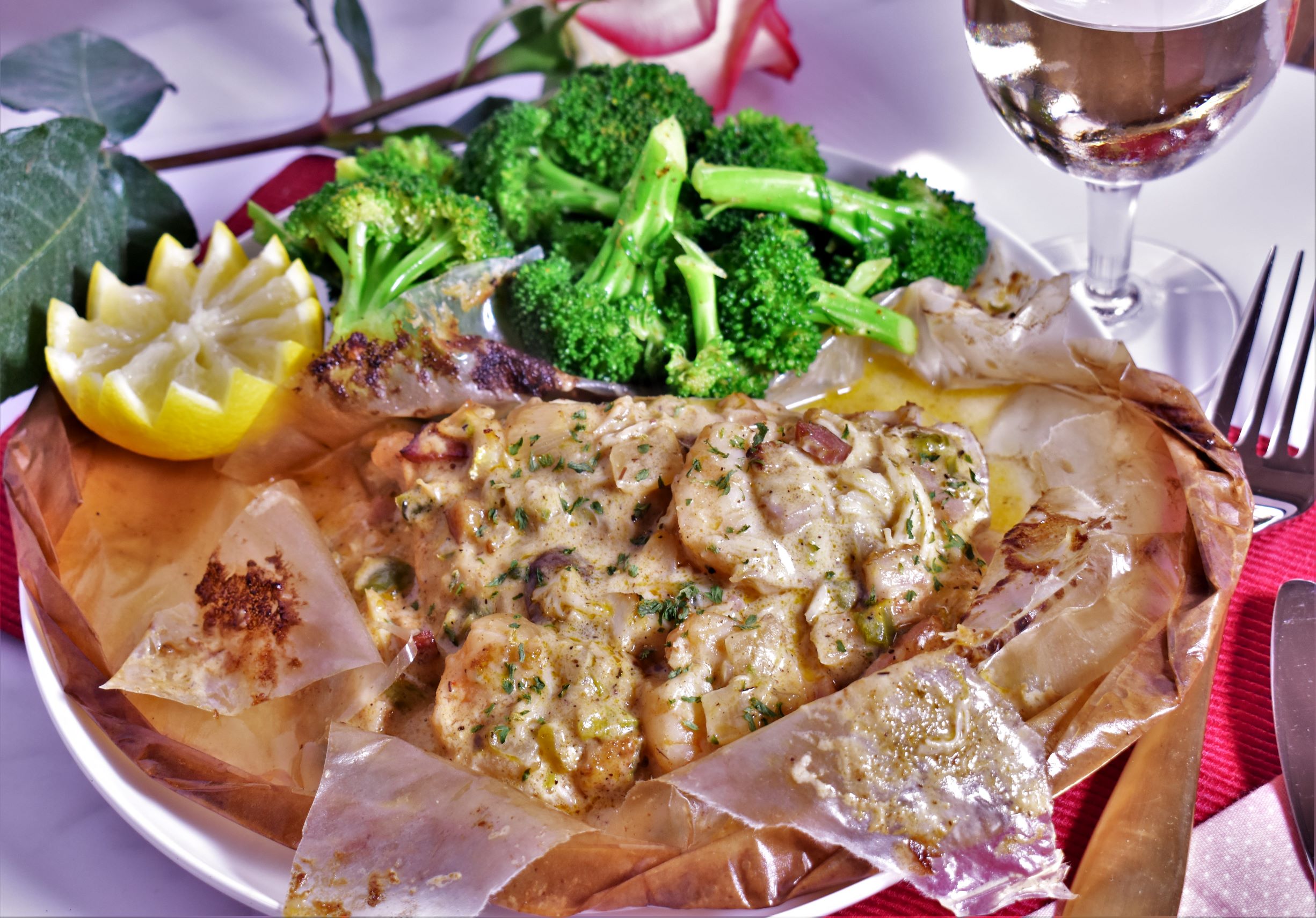 a plate of fish en papillote with a side of broccoli and a lemon slice for garnish