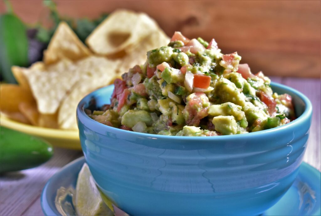 a bowl of guacamole next to a plate of chips