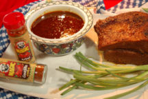 a dish full of louisiana barbeque sauce surrounded by2 containers of magic arbol and guajillo chile pepper, whole green onions and a peice of meat