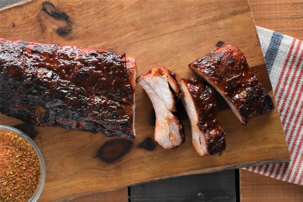 a slab of oven roasted barbeque ribs on a cut board with some ribs cut off the slab