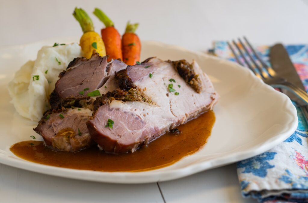 a plate with roasted pork loin with gingersnap gravy with a side of mashed potatoes and vegetables