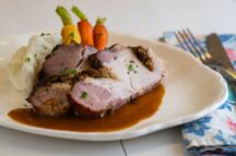 a plate with roasted pork loin with gingersnap gravy with a side of mashed potatoes and vegetables