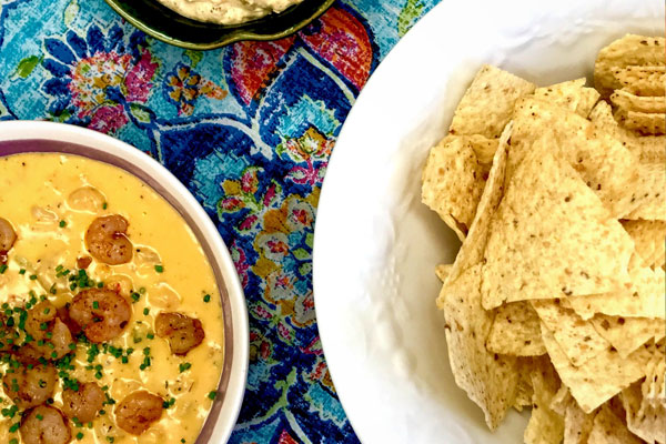 a bowl of Seafood Queso dip next to a big plate full of tortilla chips