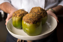 a chef holding a plate of 3 big stuffed bell peppers