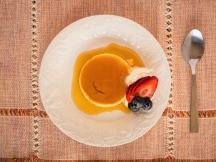 a plate with basic caramel custard on it with a side of strawberries and bludeberries