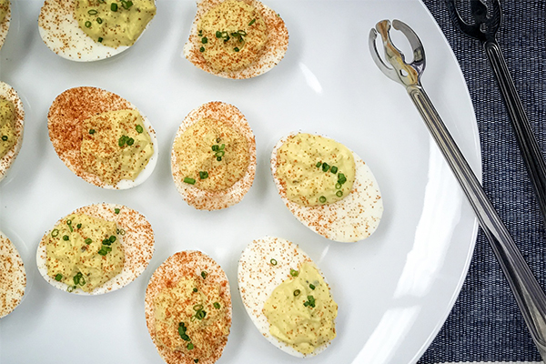 a plate full of deviled eggs next to a pair of tongs used to grab them