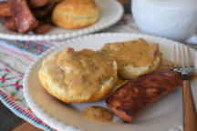 an opened biscutt with andouille cream gravy on it and a peice of breakfast sausage