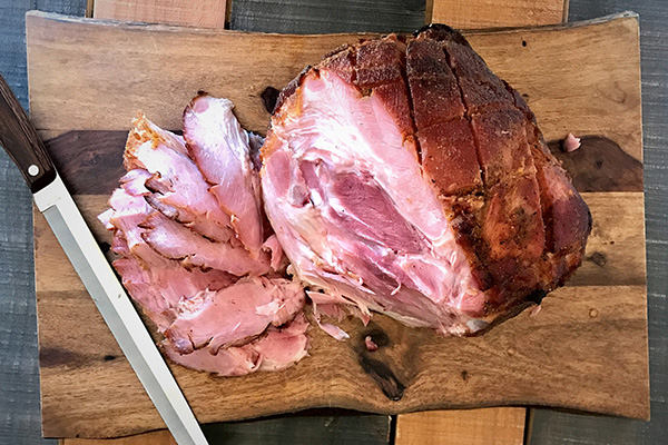 a glaxed ham on a cut board with slices cut out