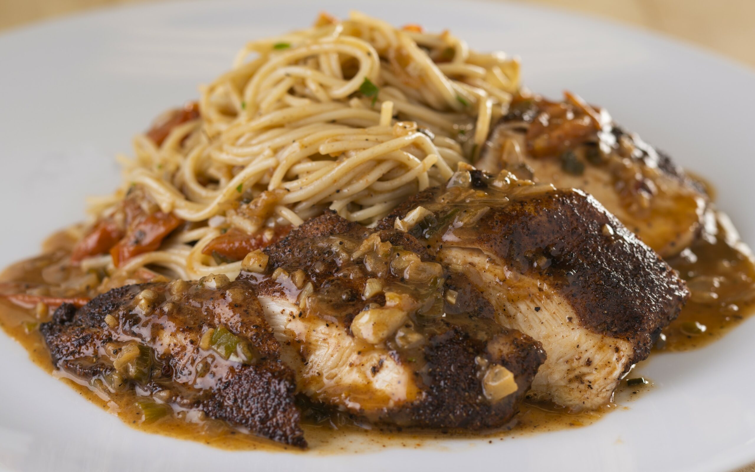 a close up of jerk chicken with tomato garlic butter sauce and some noodles