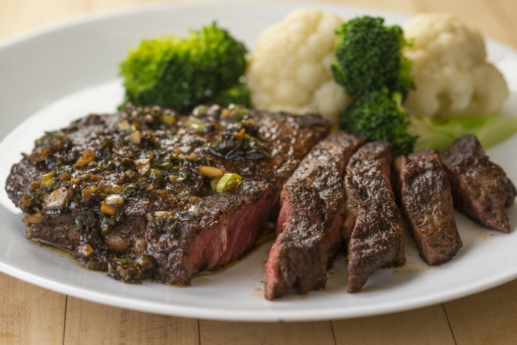 a plate with a piece of jerk ribeye cooked medium well 4 pieces cut out with a side of mashed potatoes and broccoli