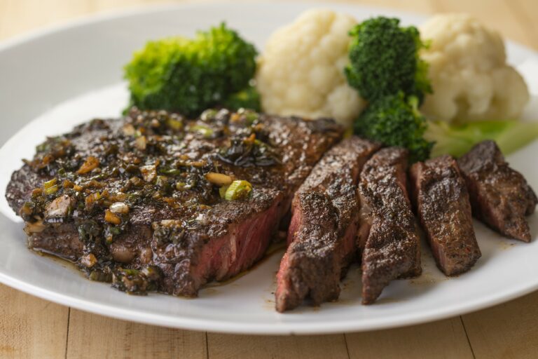 a plate with a piece of jerk ribeye cooked medium well 4 pieces cut out with a side of mashed potatoes and broccoli