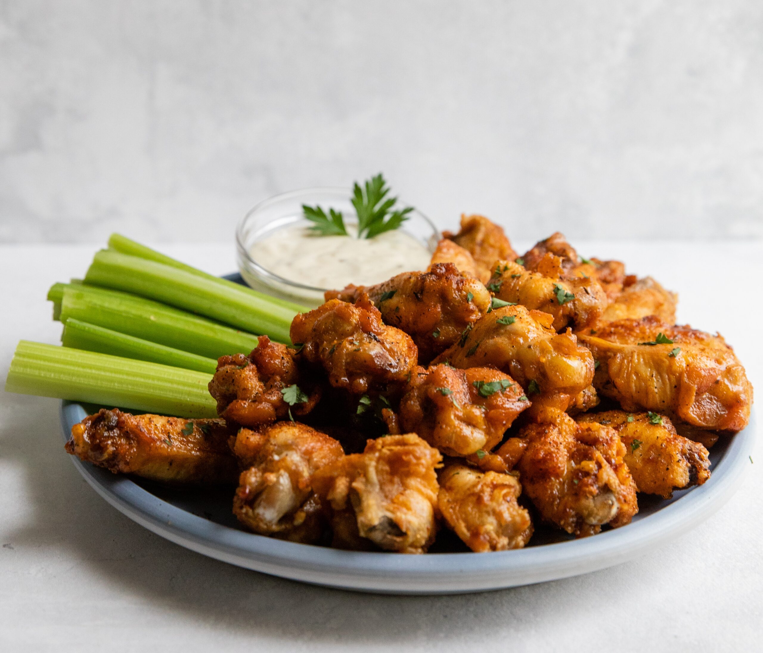 a plate of magic buffalo wings with a cup of dipping sauce and celery