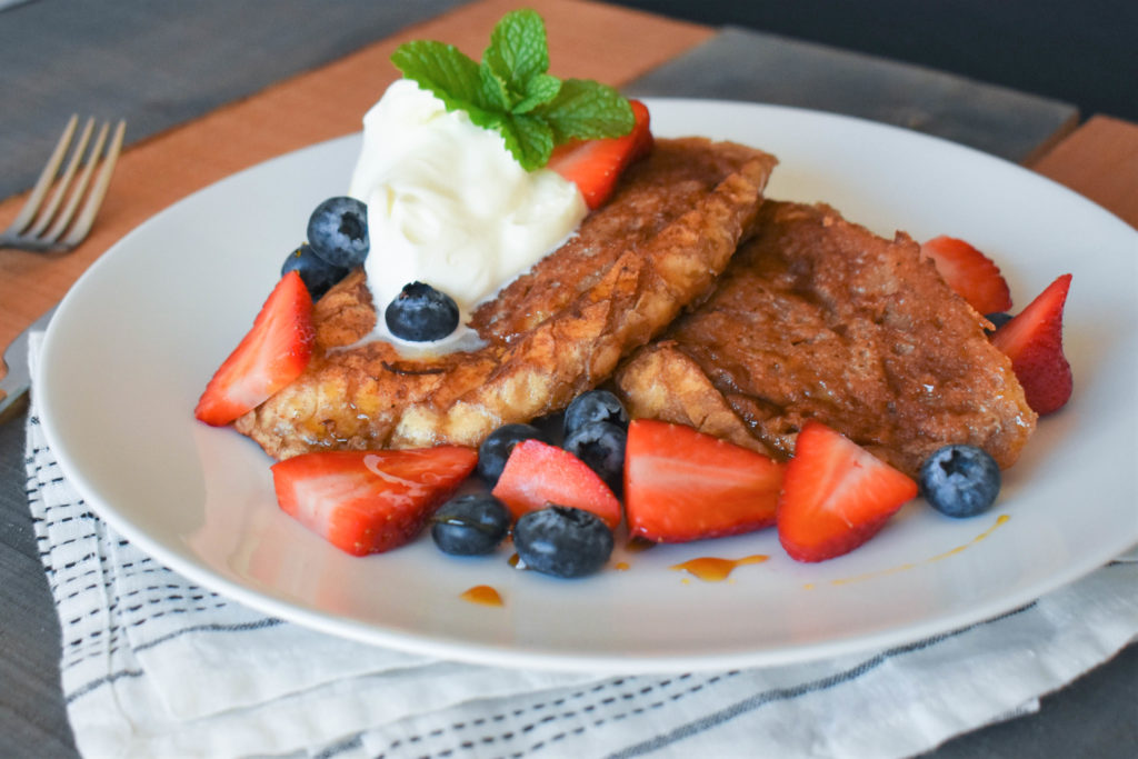 a plate of Pain Perdu topped with whipped cream and blueberries and strawberries