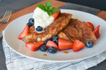 a plate of Pain Perdu topped with whipped cream and blueberries and strawberries
