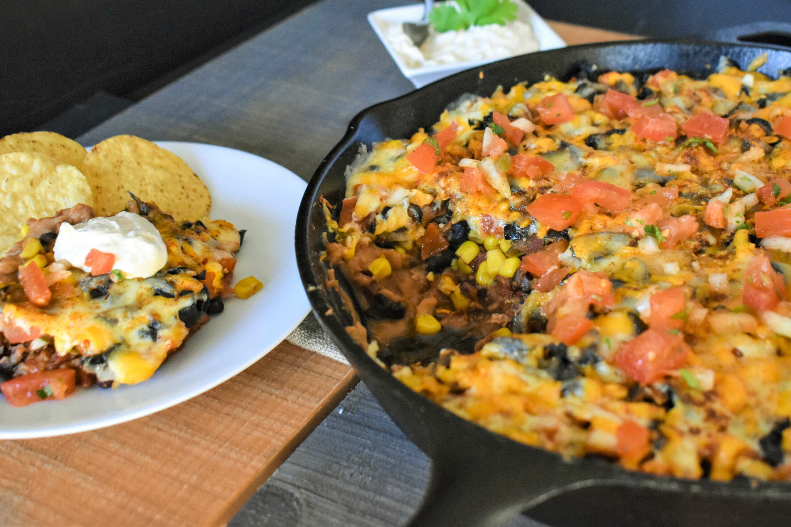 a cast iron skillet of fajita magic Seven Layer Dip next to a plate of chips and the dip