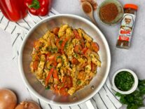 chicken fajitas on a white plate next to magic seasoning, cilantro, bell peppers and onions