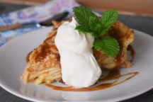 a piece of caramel apple pie on a plate with a scoop of whipped cream on top