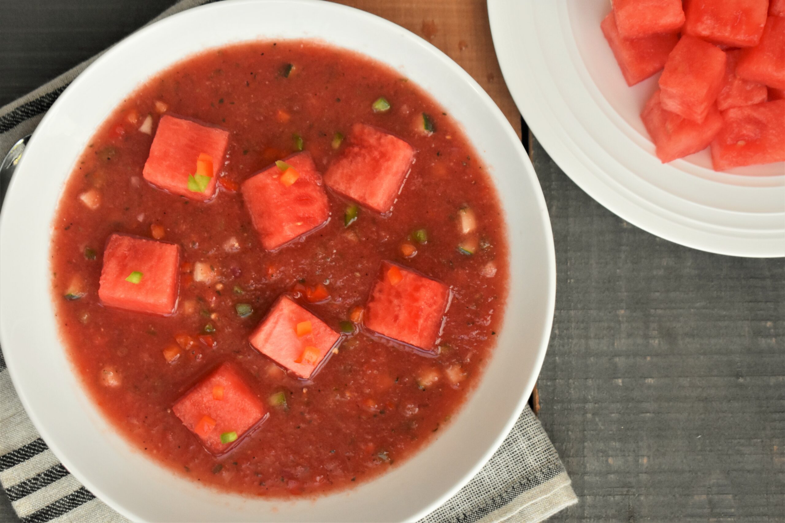 a plate of watermelon gazpacho next to a plate of cut watermelon