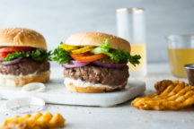 2 meat magic burgers fully dressed on a chop board with waffle fries around them