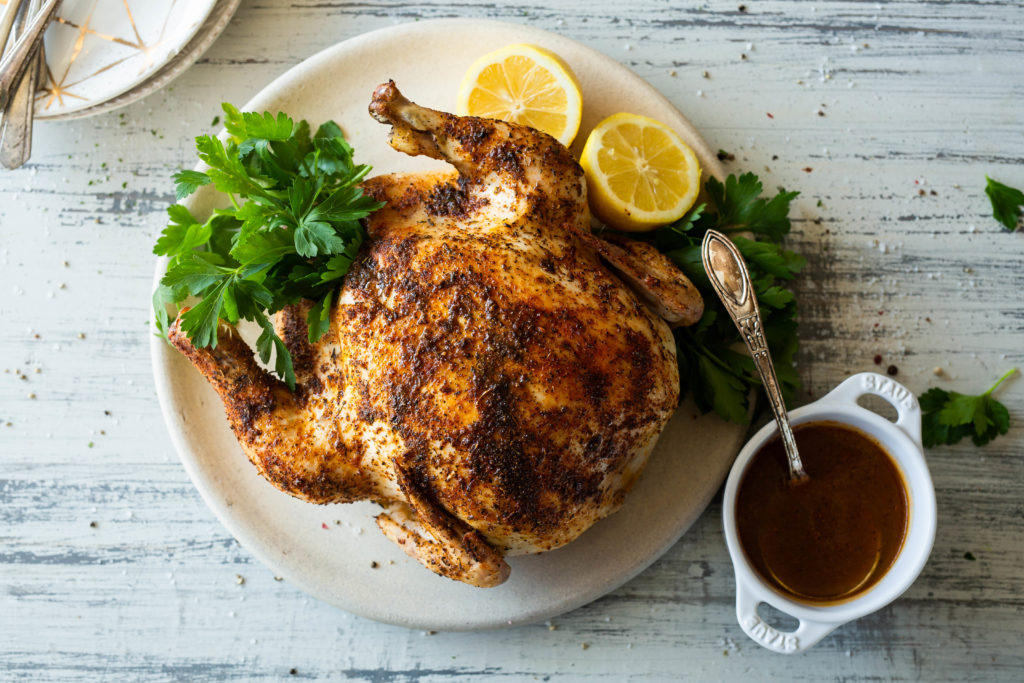 a plate with a roasted chicken next to a cup of cajun jus