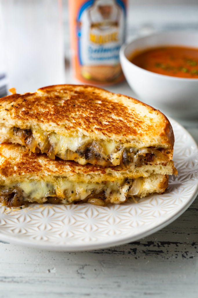 a salmon magic grilled cheese sandwich cust in half and stacked on top of eachother next to a bowl of soup in the background