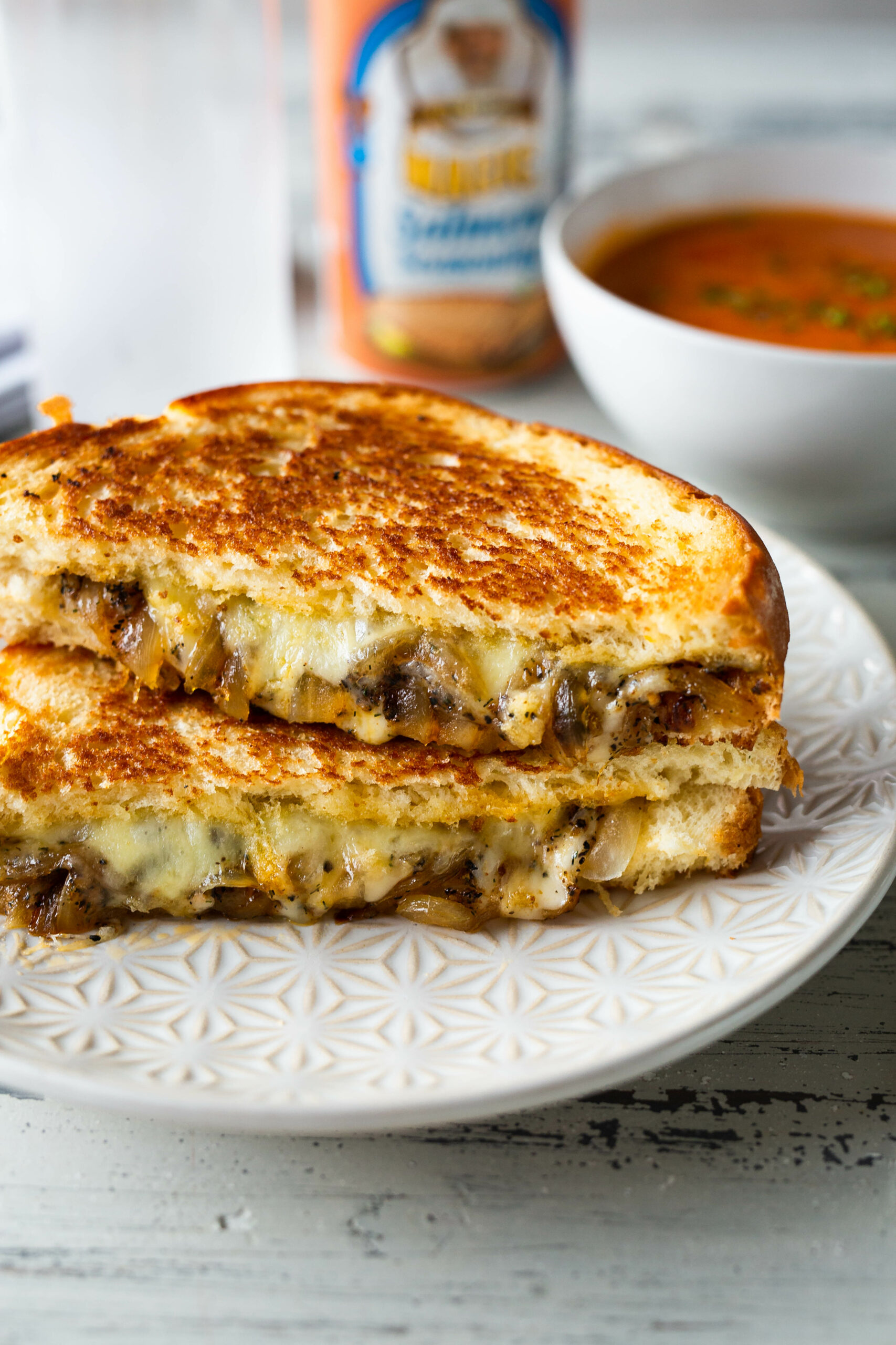 a salmon magic grilled cheese sandwich cust in half and stacked on top of eachother next to a bowl of soup in the background