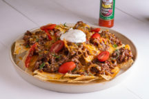 a palte of fajita beef nachos topped with sliced cherry tomates and a dollap of sour cream