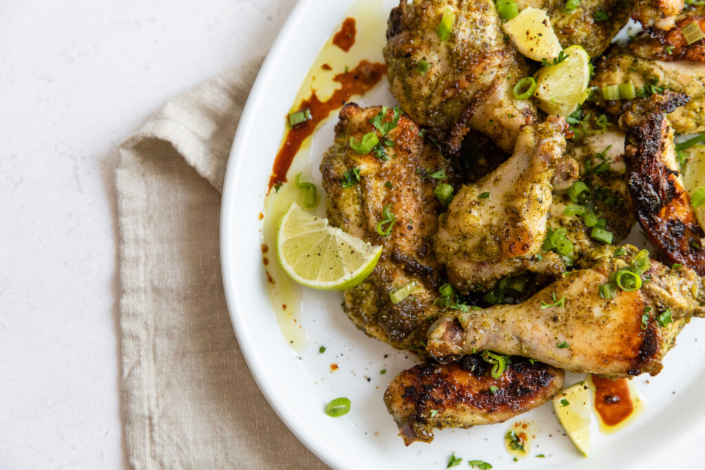 Grilled chicken wings with herb seasoning and lemon wedges on a white plate, garnished with chopped green onions and served on a beige linen napkin.