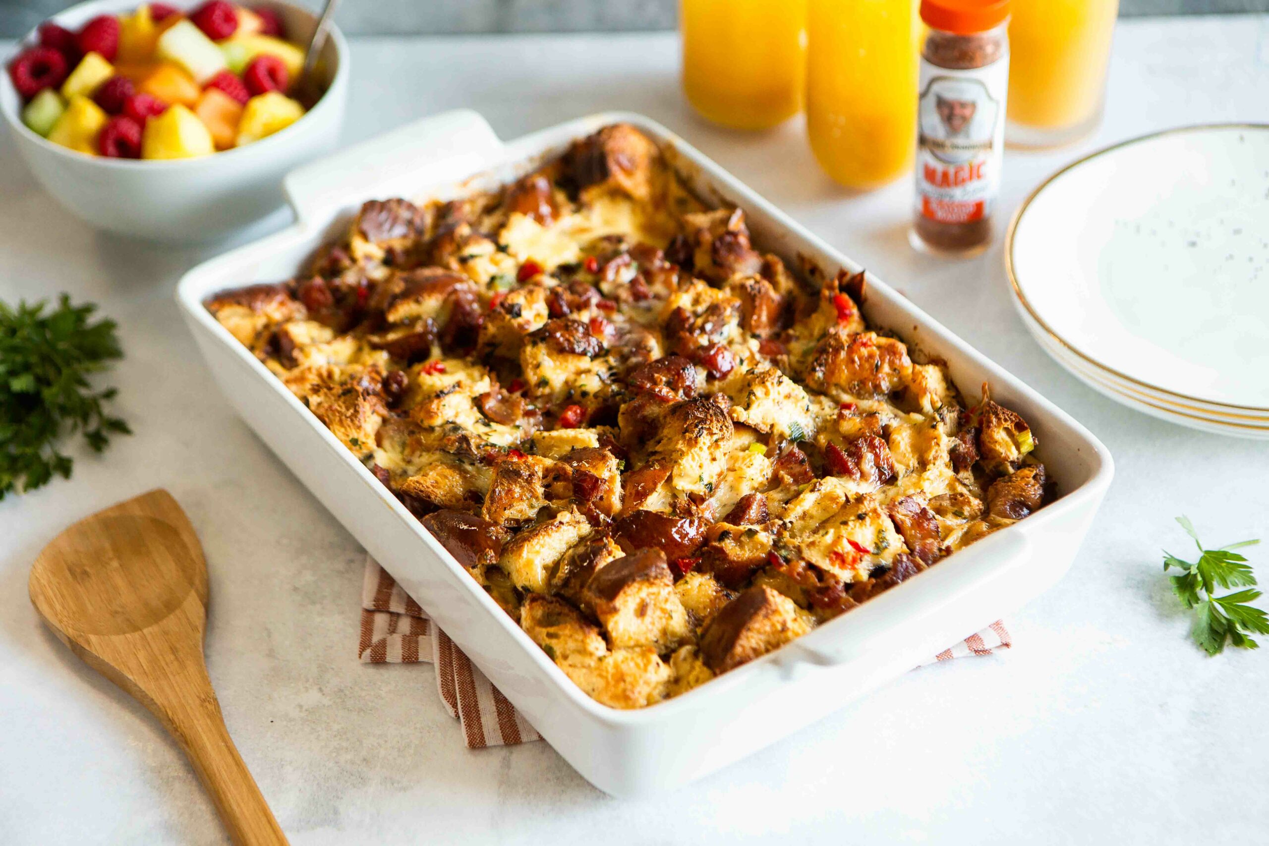 a dish of strata next to a bowl of mixed fruits